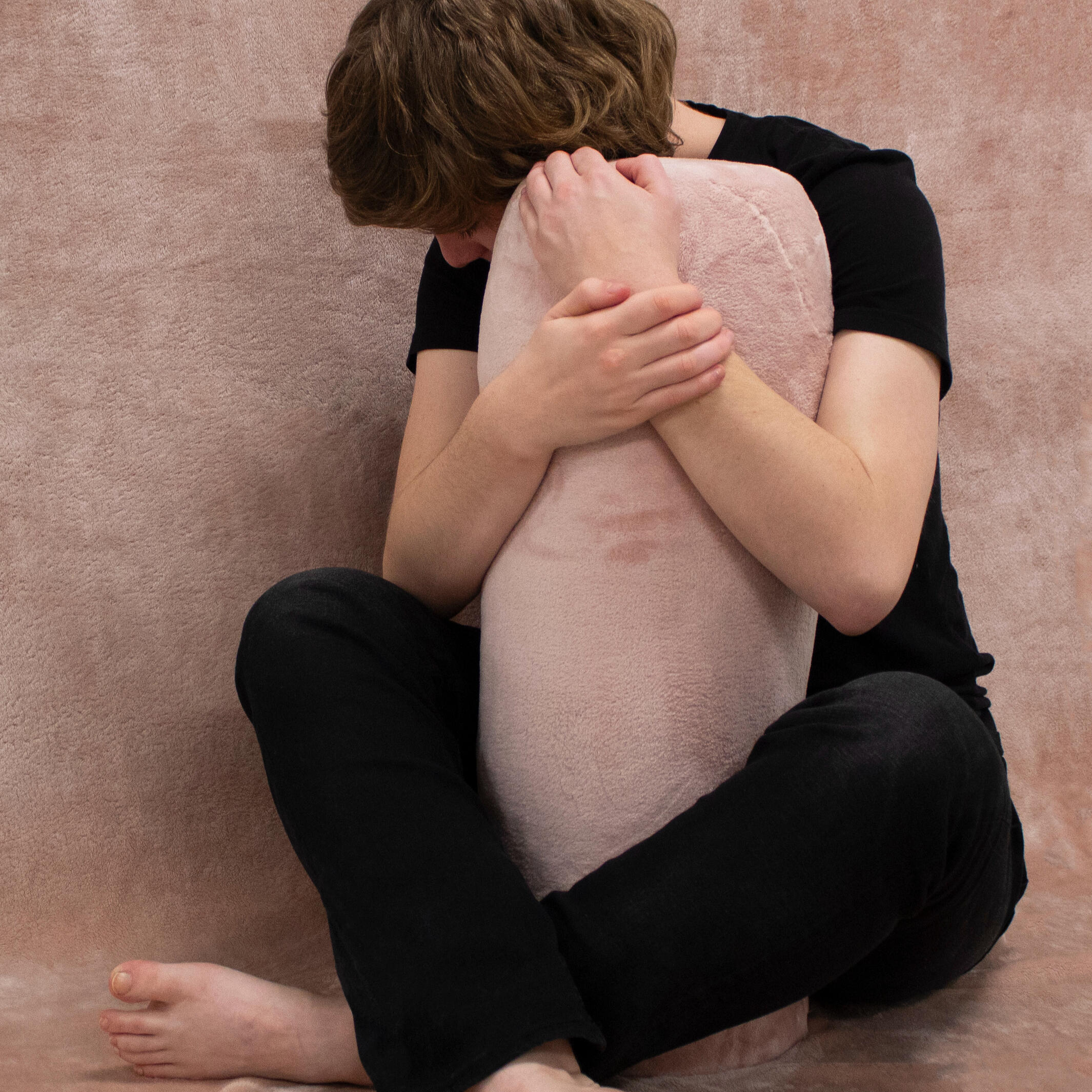 A person wearing black clothing sits behind and hugs a ceramic form covered in a fuzzy pink skin against a pink background. Made by Mia Donalson.