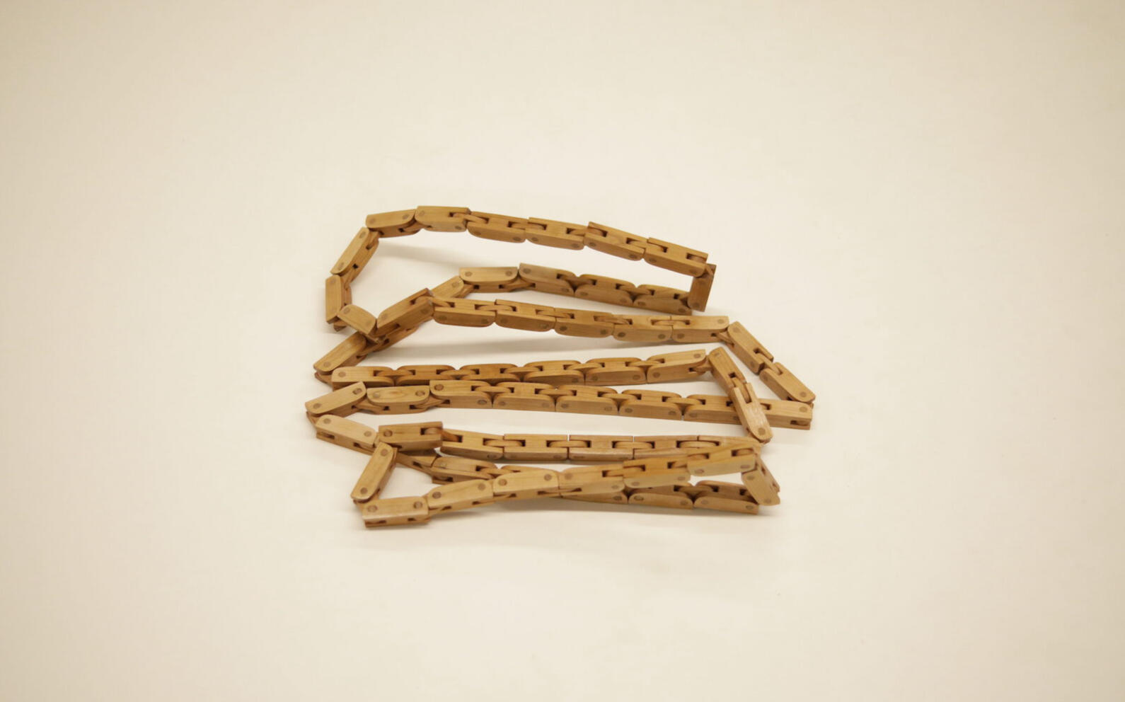 A wooden articulated chain handcrafted from cherry wood sits in a pile on a white background. Made by Mia Donalson.