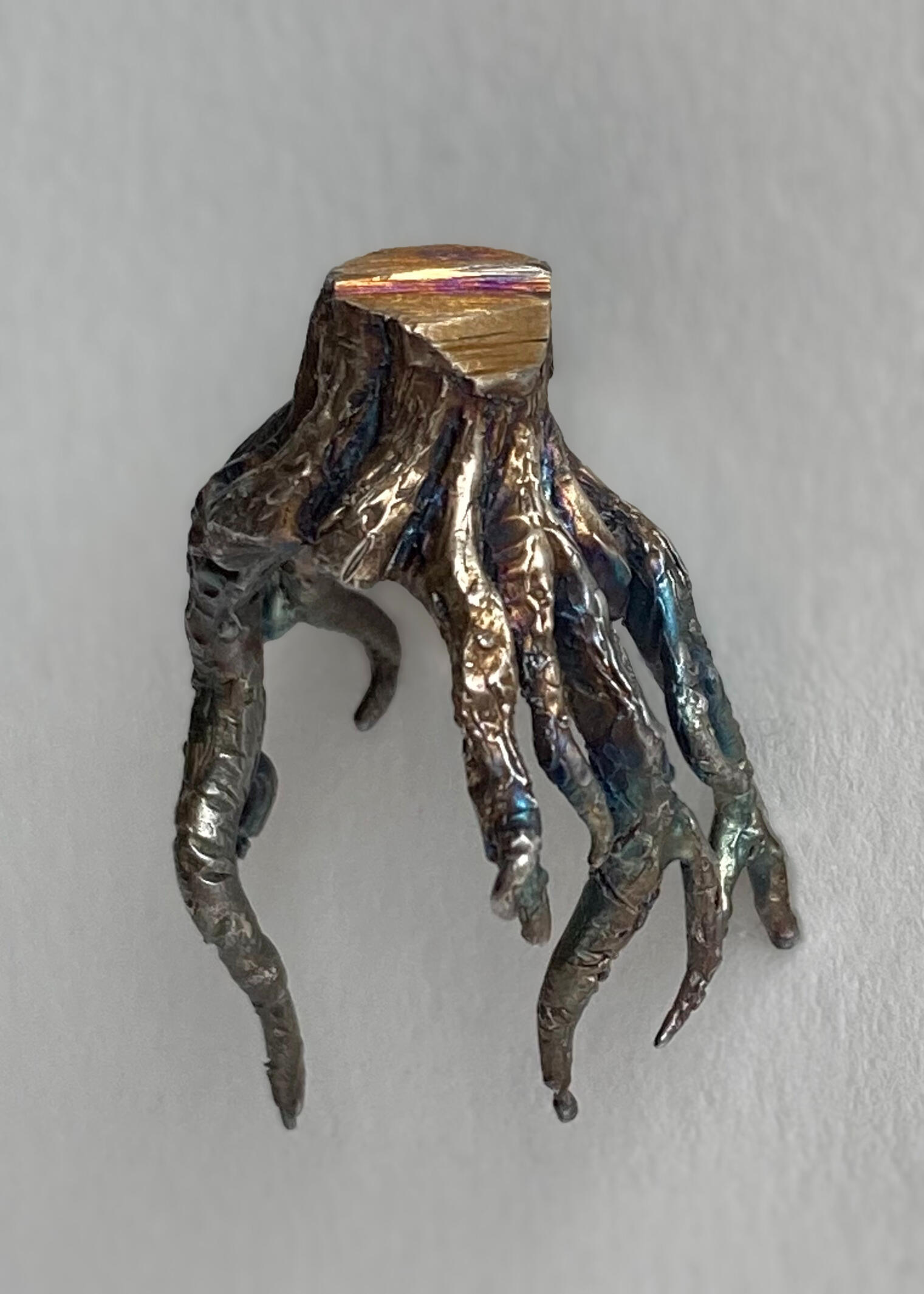 A handcrafted cast ring cast in silver is shown against a white background. The ring is in the shape of a stump with the roots extending down and finishes with a liver of sulfur patina. made by Mia Donalson.