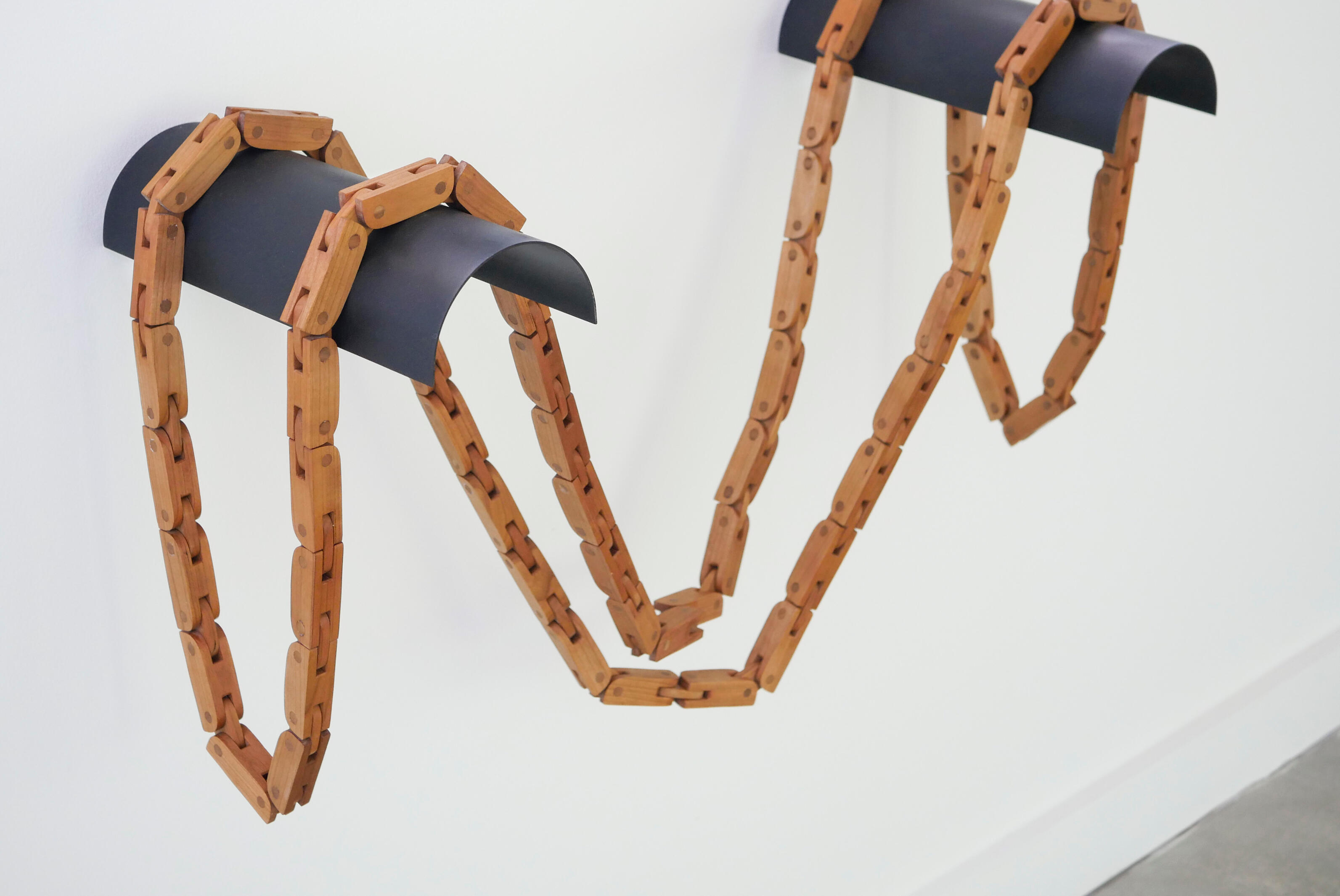 A wooden articulated chain handcrafted from cherry wood sits in a pile on a white background. Made by Mia Donalson.