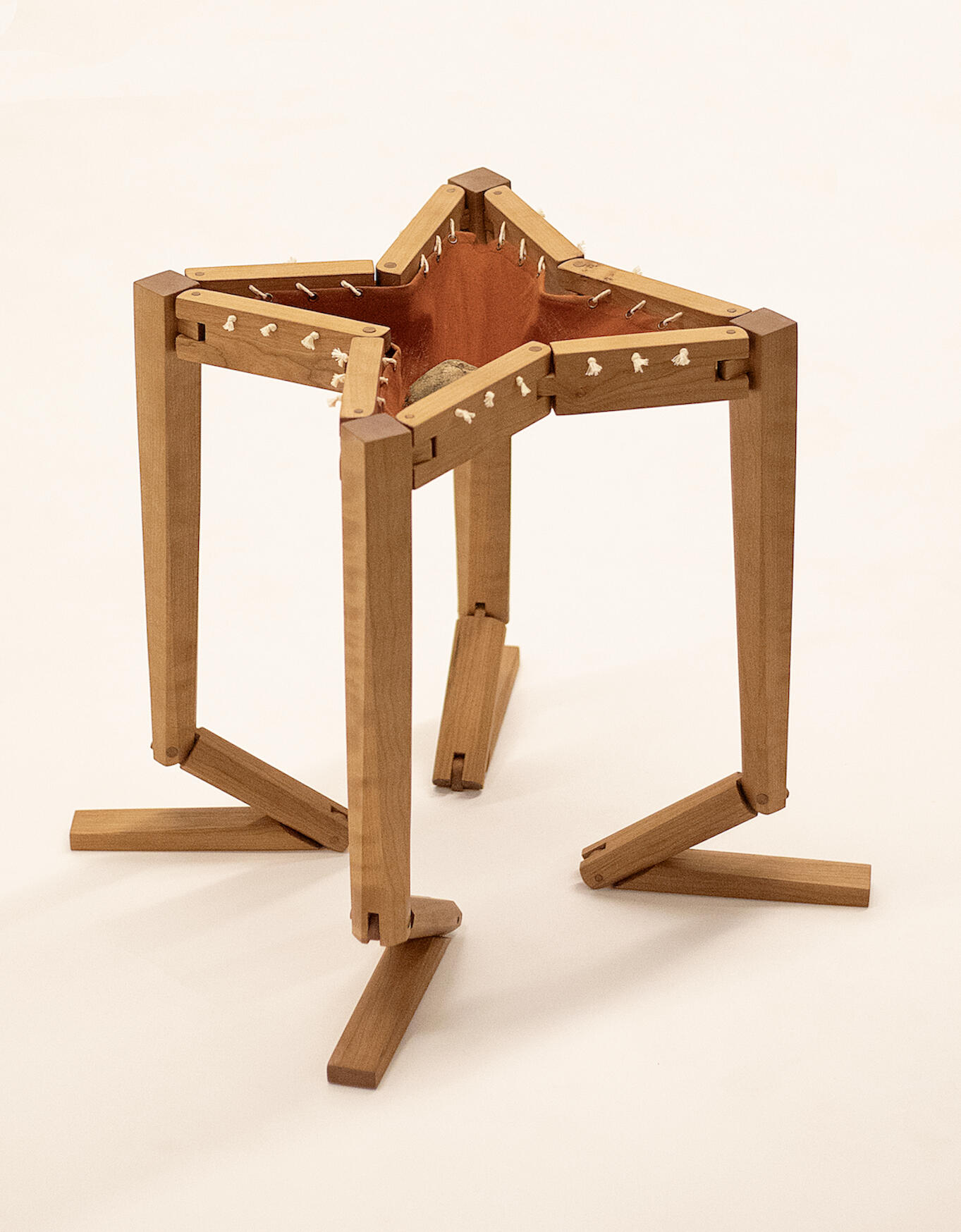 A handcrafted table made from cherry wood shown against a white background kneeling with a rock in the orange-brown cotton fabric top. Made by Mia Donalson.