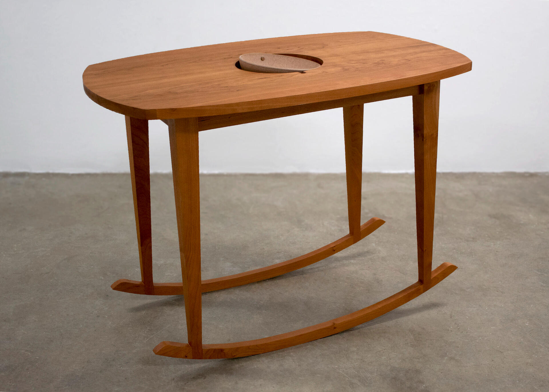 This is a wooden table with rockers made by Mia Donalson. It has a ceramic bowl in the center of it.