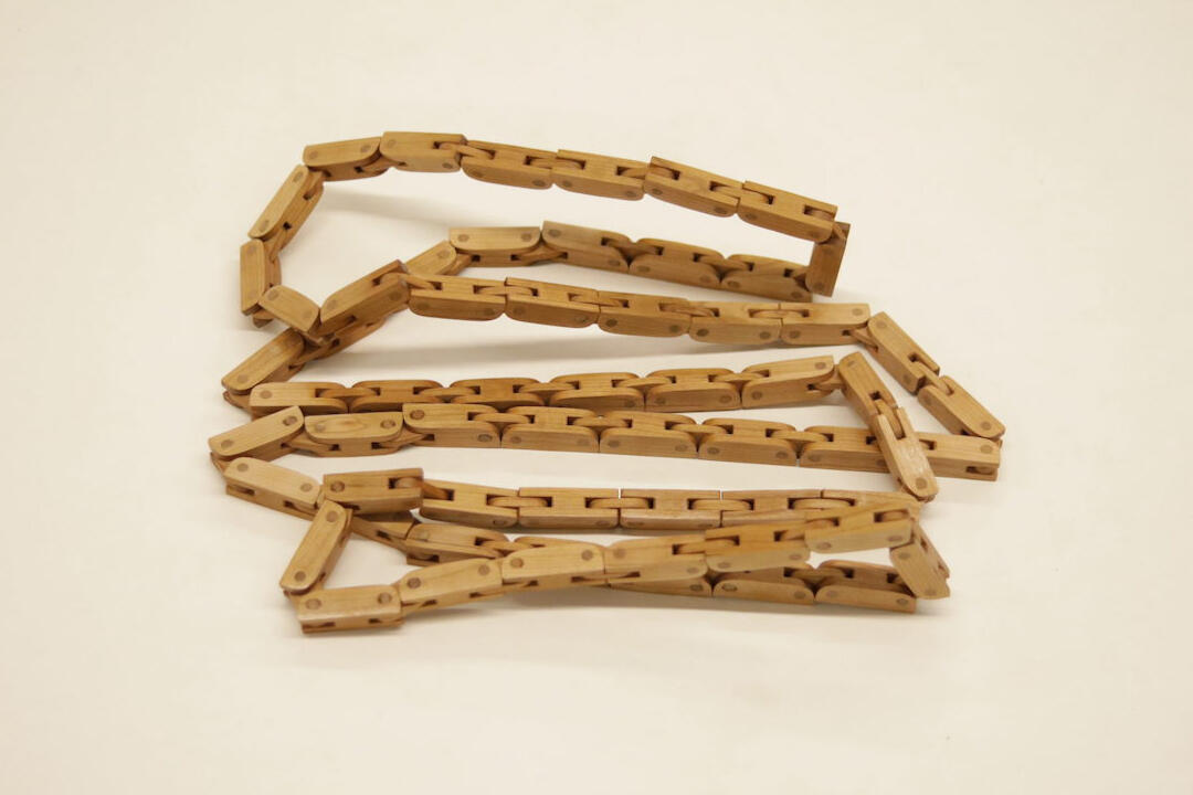 A wooden articulated chain handcrafted from cherry wood sits in a pile on a white background. Made by Mia Donalson.