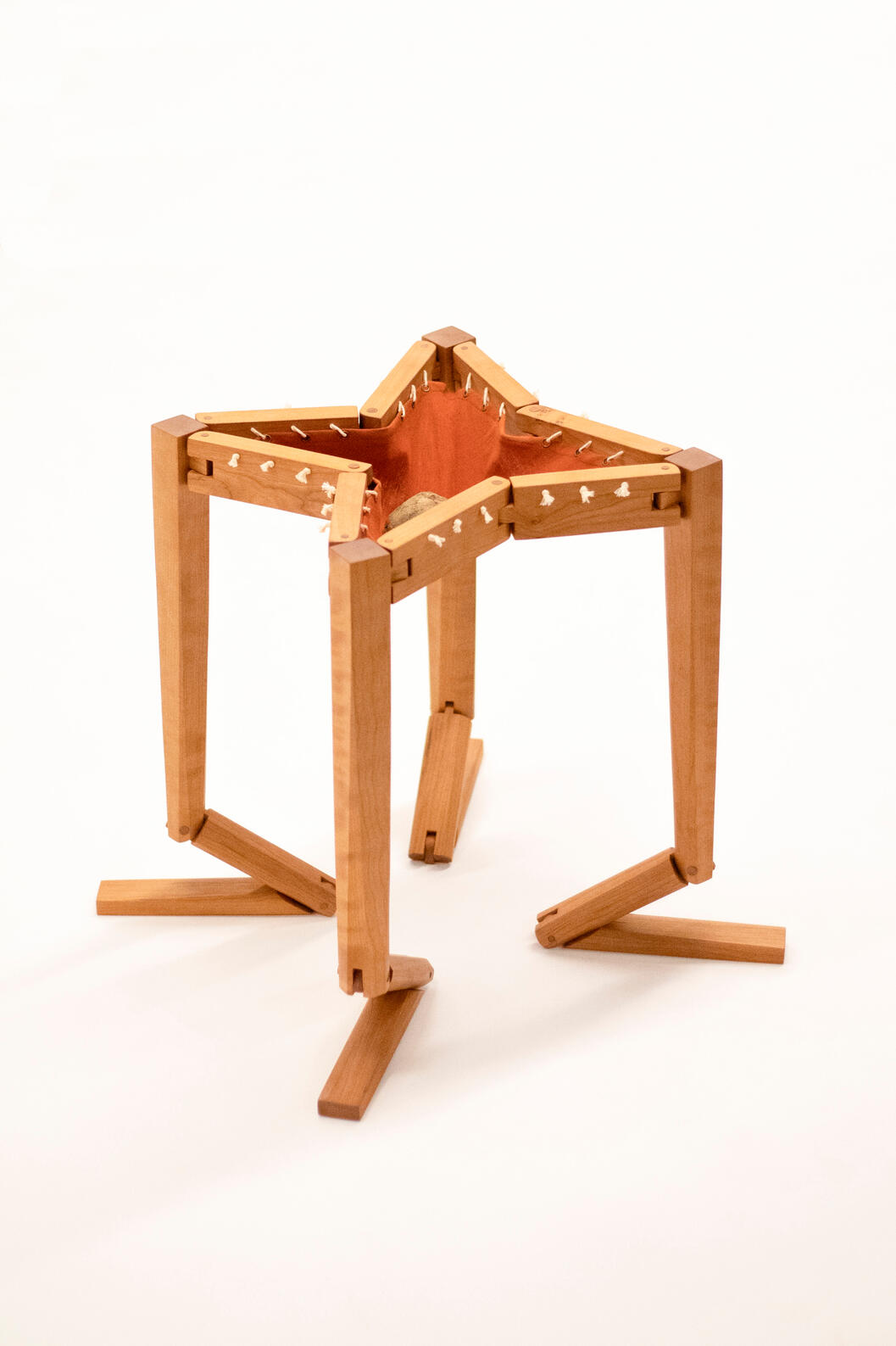 A handcrafted table made from cherry wood shown against a white background kneeling with a rock in the orange-brown cotton fabric top. Made by Mia Donalson.